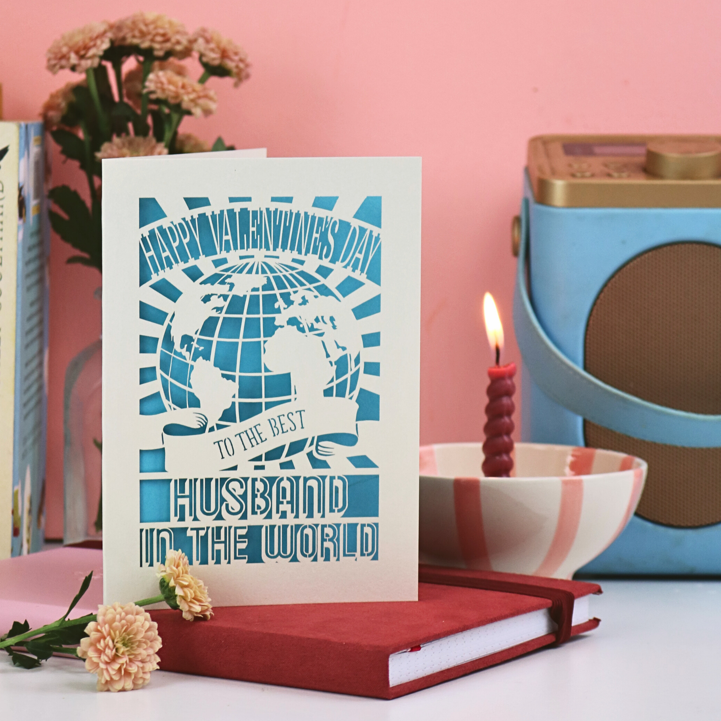 A laser cut husband Valentine's card on a desk with flowers, radio, candle and books. Card says "Happy Valentine's Day to the best husband in the world"