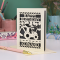 Personalised husband Birthday card with grey and cream design featuring a tractor and balloons, with 'Happy Birthday Edward' text, on a desk with stationery items.