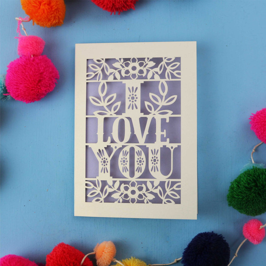 Cut out Valentine's Card with 'I LOVE YOU' design surrounded by colourful pom-poms on a blue background