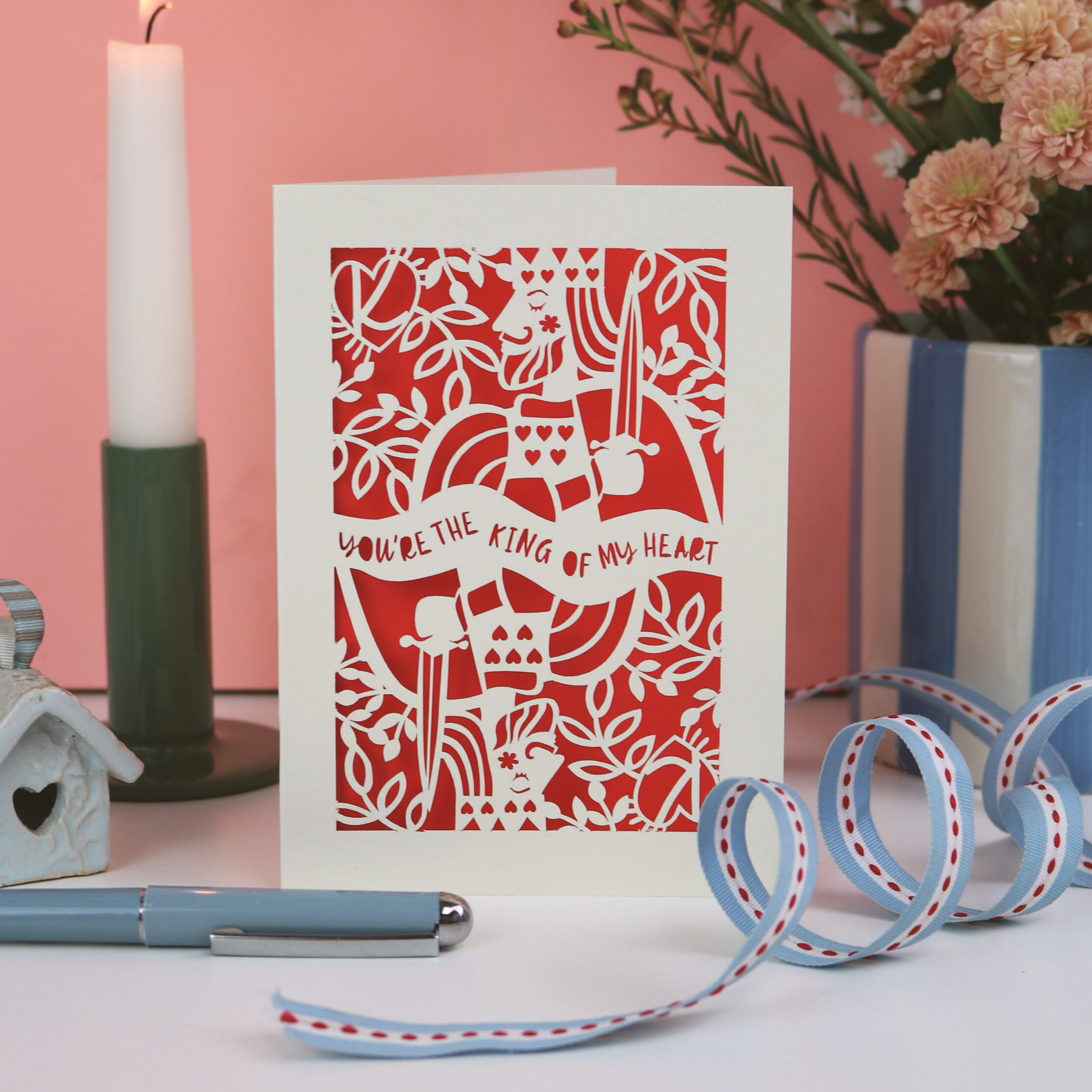 Laser cut Valentines card with decorative King of Hearts design and text, "You're the king of my heart", placed on a surface with a pen and decorative items.