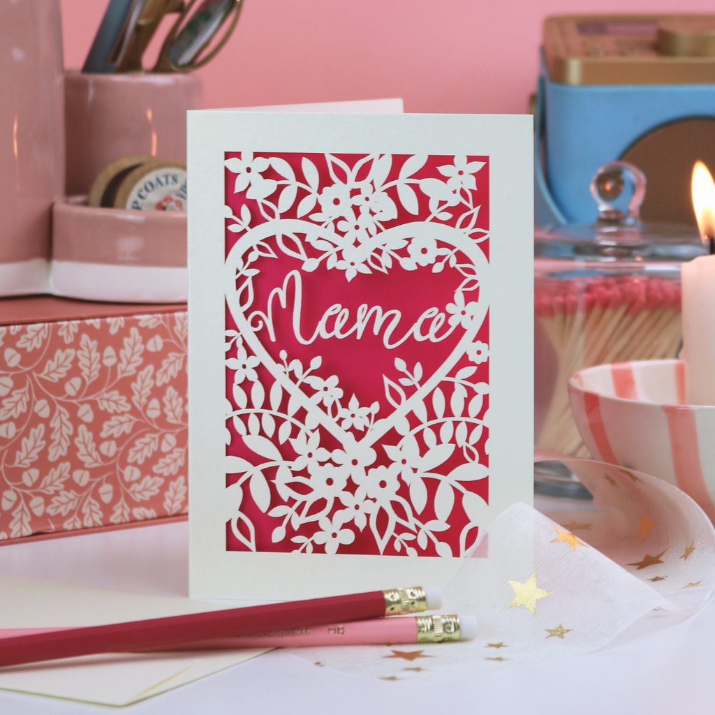 A cream and shocking pink laser cut card with cut out floral design and the word "Mama" in  heart shape. 