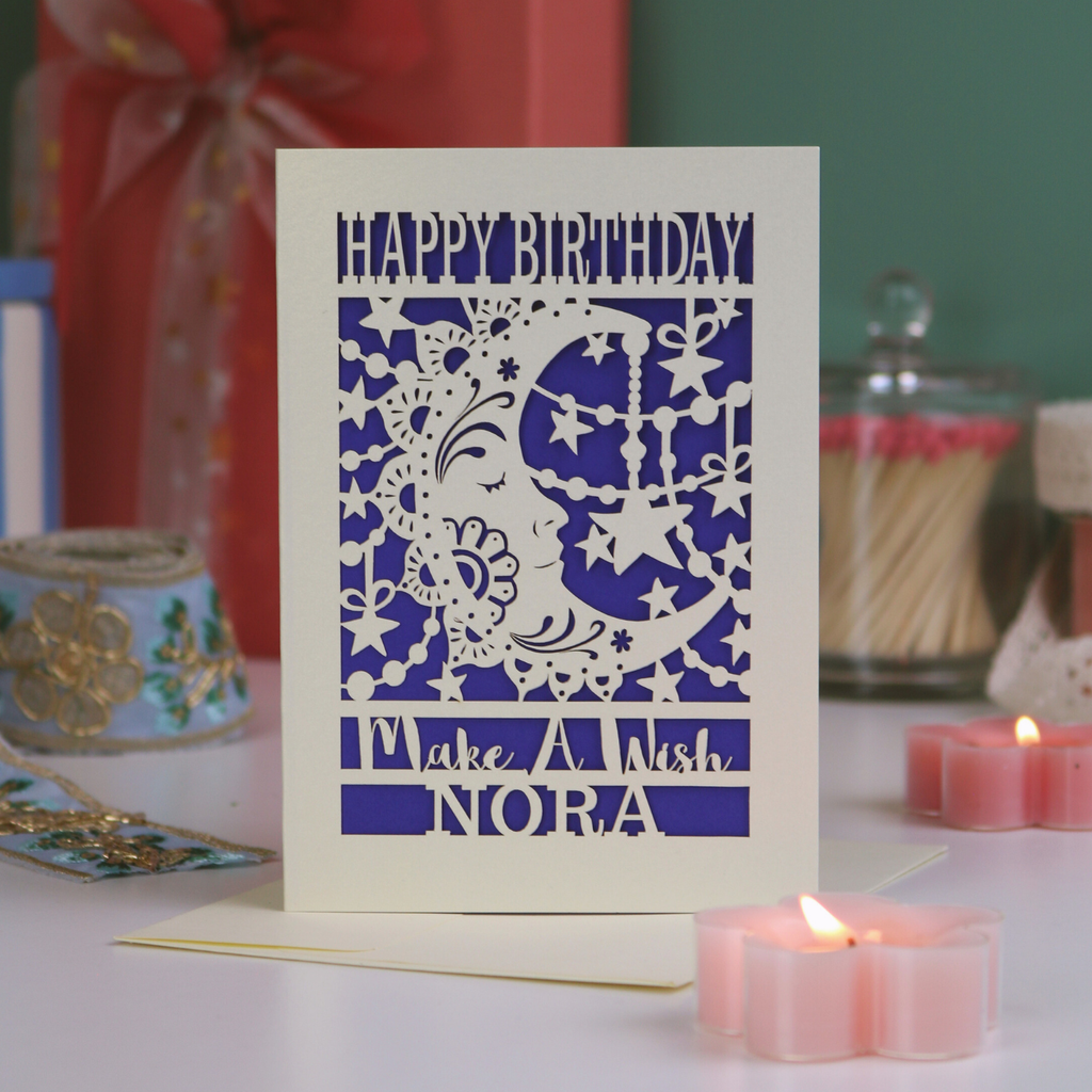 Birthday card with decorative moon and stars design on a table with candles and a gift.