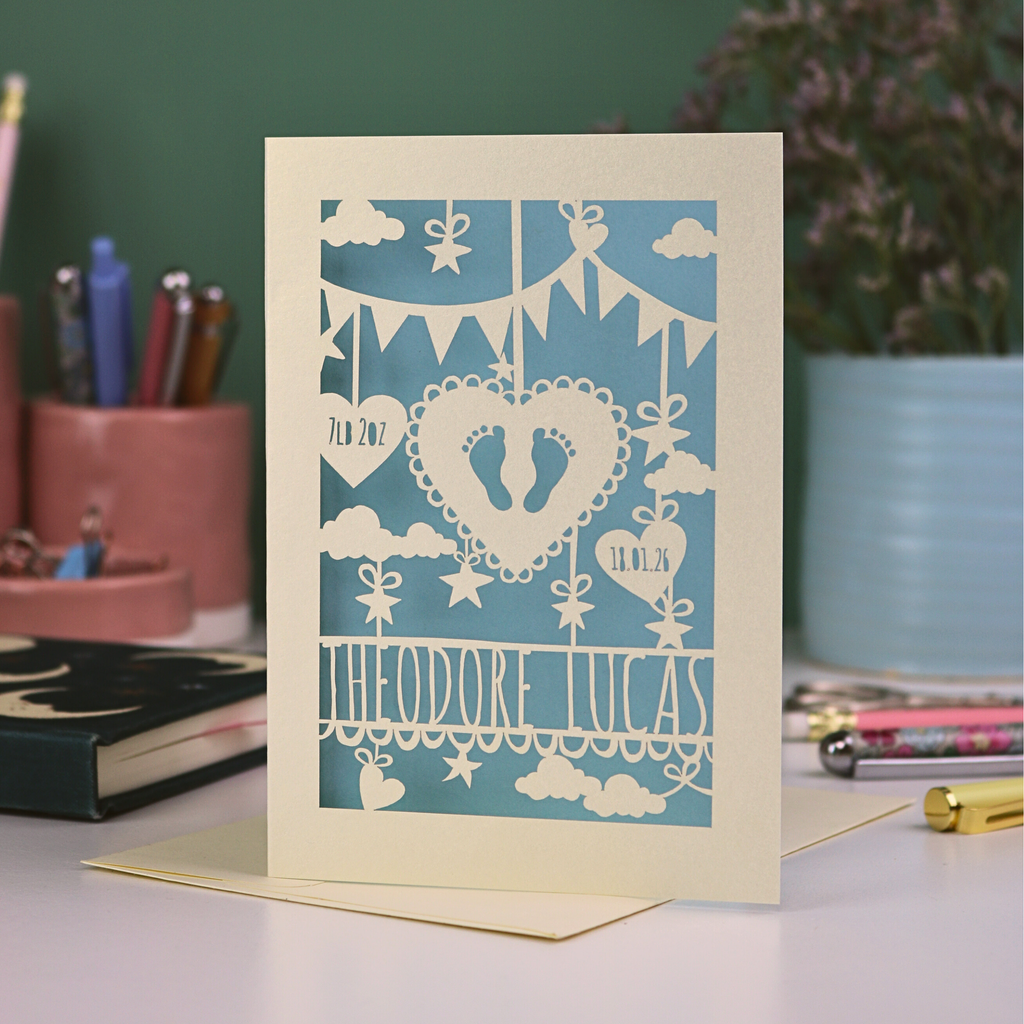 Decorative baby card with laser cut-out design on a desk with stationery items.