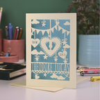 Decorative baby card with laser cut-out design on a desk with stationery items.