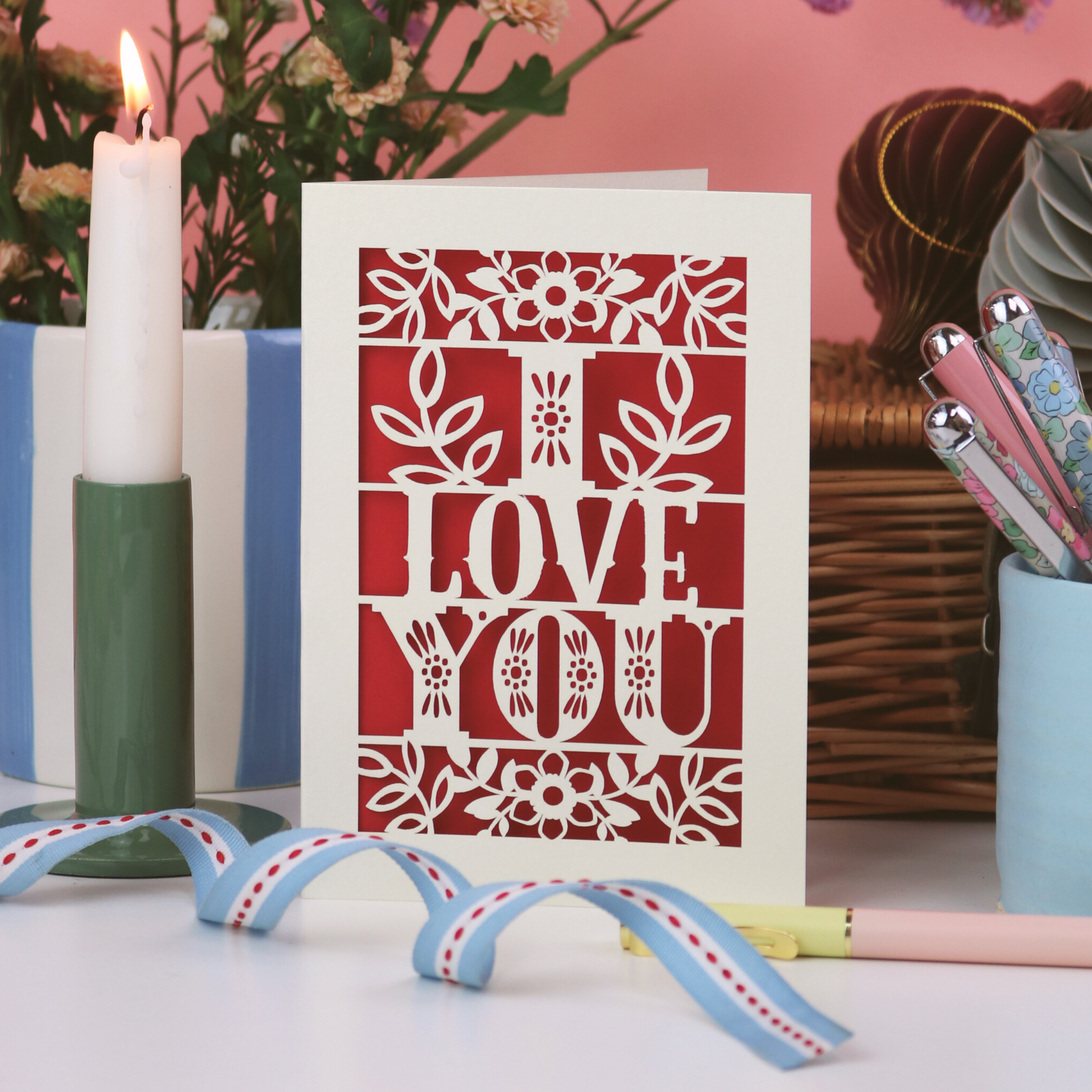 Card with 'I Love You' design on a table with candles and flowers in the background