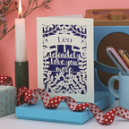 Valentines Card with 'Leo, I definitely love you more' text on a blue stand with a candle and decorative items.