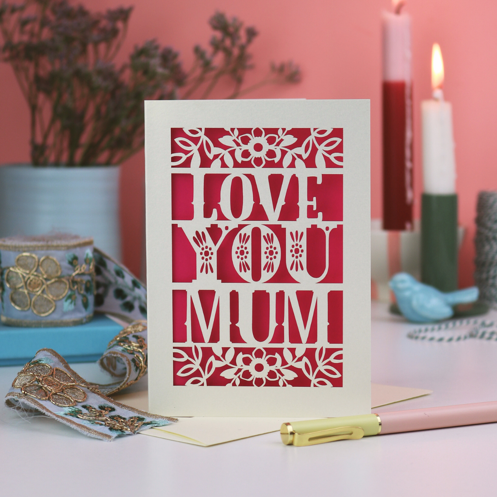 Card with 'Love You Mum' text on a decorative table with candles and flowers.