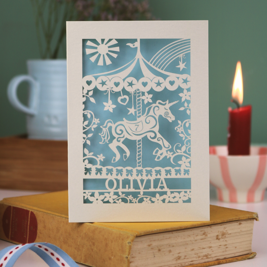 Decorative birthday card with unicorn design and a name on a book with a candle and ribbon in the background