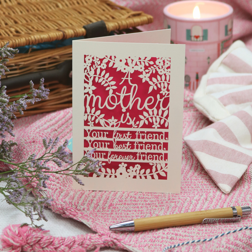 Mother's Day card with floral design and text on a pink fabric background with a candle and basket.
