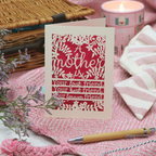 Mother's Day card with floral design and text on a pink fabric background with a candle and basket.