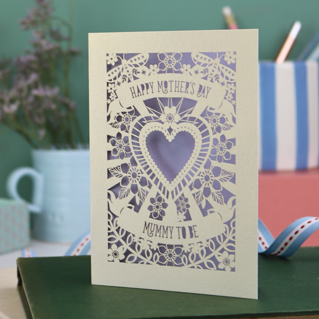 Card with floral design and 'Happy Mother's Day' text on a green surface with stationery items.
