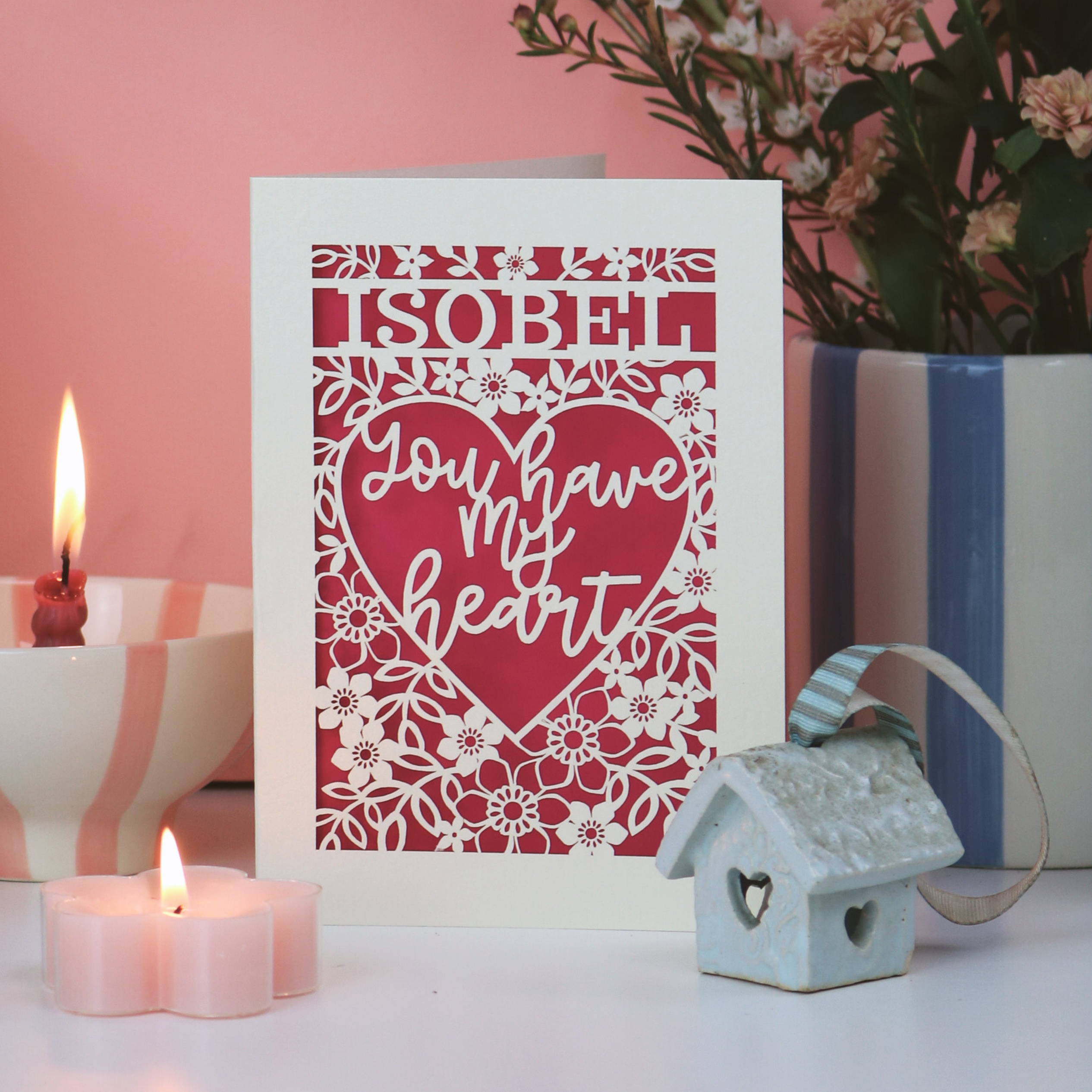 Laser cut Valentine's Card with 'ISOBEL You have my heart' text on a decorative surface with candles and flowers.