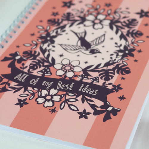 A wire bound A5 notebook with pink striped cover and purple floral illustrations, and the text "All of my Best Ideas"