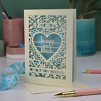 Laser-cut vow renewal card with personalized text on a table with stationery items.