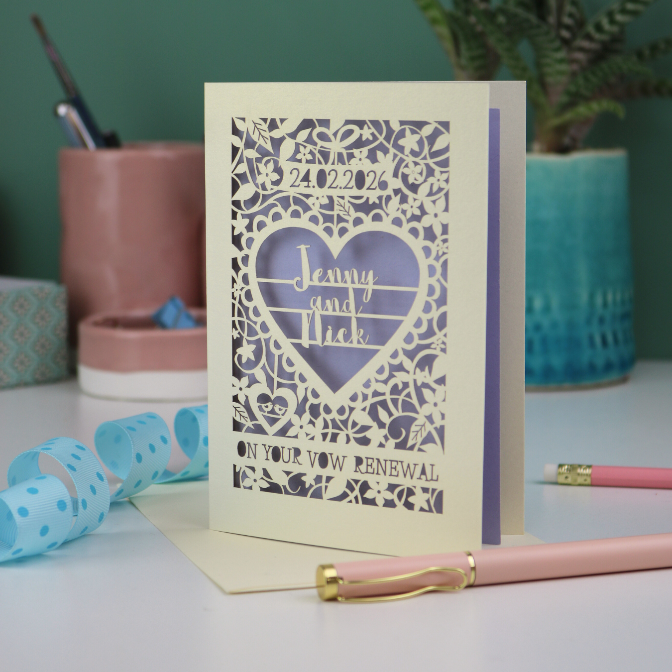 Laser-cut card for a vow renewal with personalized text on a desk with stationery items.