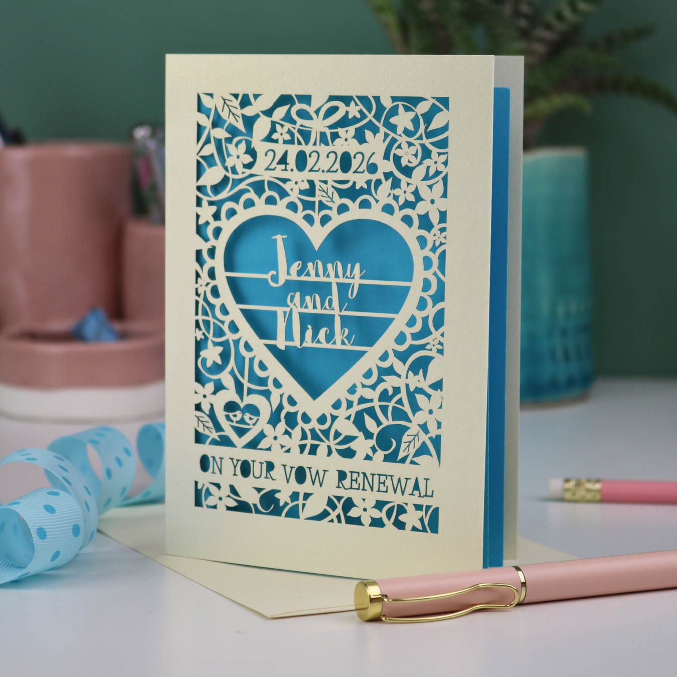 Personalized vow renewal card with decorative heart design on a table with stationery items.
