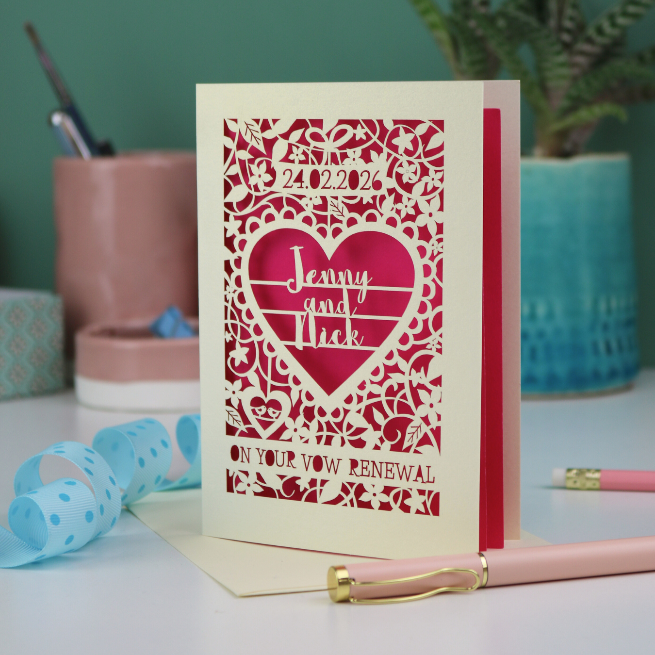 Personalised cut out vow renewal card with decorative heart design on a table with stationery items.