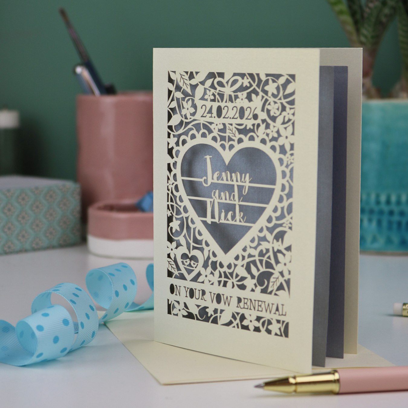 Decorative wedding vows renewal card with laser cut heart design on a table with stationery items.