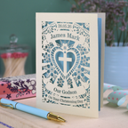 Personalised Paper cut Godson Christening card with decorative elements on a wooden surface.
