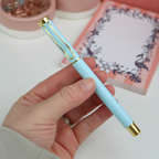 Hand holding a light blue pen with gold accents, blurred background