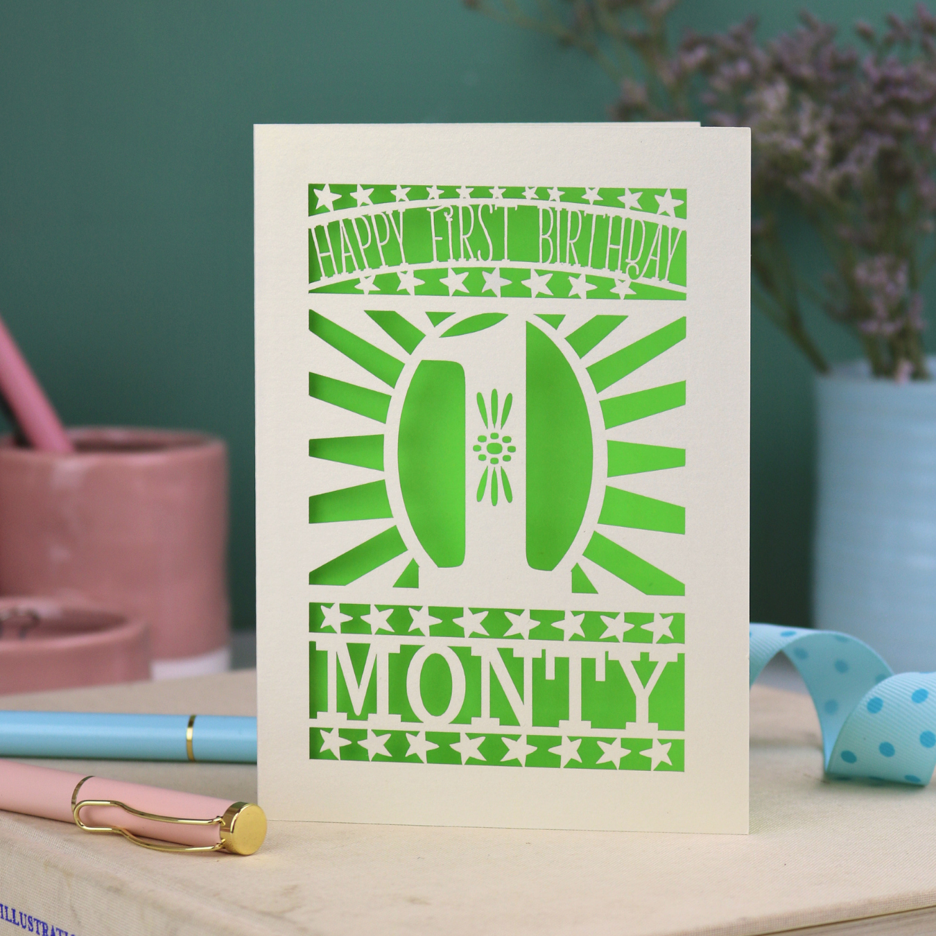 Personalised Baby's 1st Birthday card. laser cut with star borders and "Happy First Birthday" at the top, a decorative cut out number 1 in the centre and personalised with the name "MONTY" at the bottom. card is cream with a bright green paper backing
