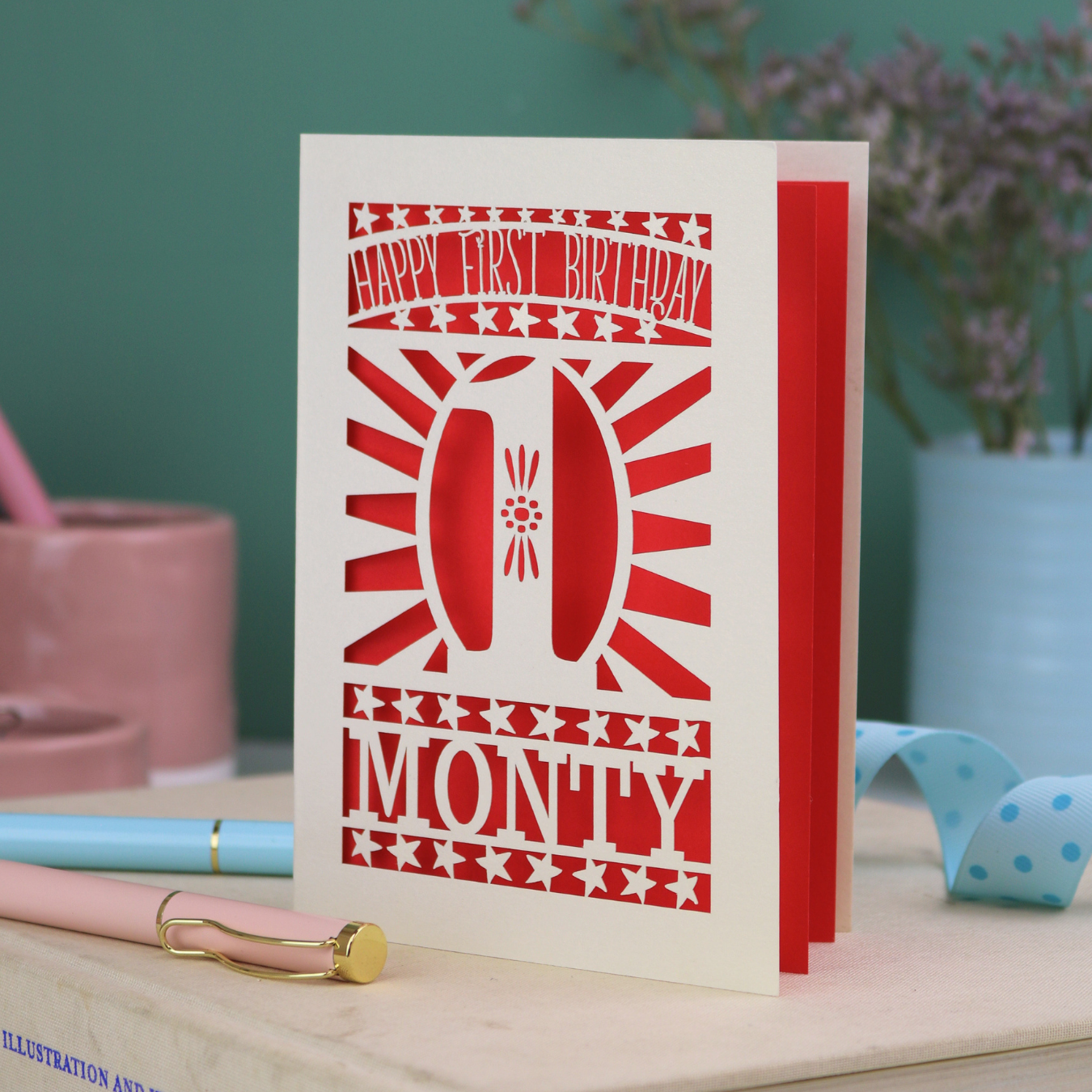 Personalised Baby's First Birthday card. laser cut with star borders and "Happy First Birthday" at the top, a decorative cut out number 1 in the centre and personalised with the name "MONTY" at the bottom. 