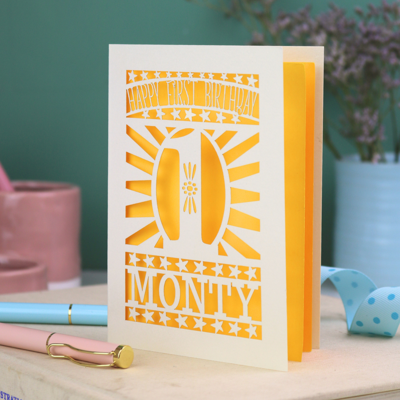 Personalised Baby's 1st Birthday card. laser cut with star borders and "Happy First Birthday" at the top, a decorative cut out number 1 in the centre and personalised with the name "MONTY" at the bottom. card is cream with a bright yellow paper backing