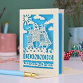 A laser cut boys birthday card with cut out pirate ship design, personalised with the name "Connor". Card stands on a white desk with a pen and stationery items