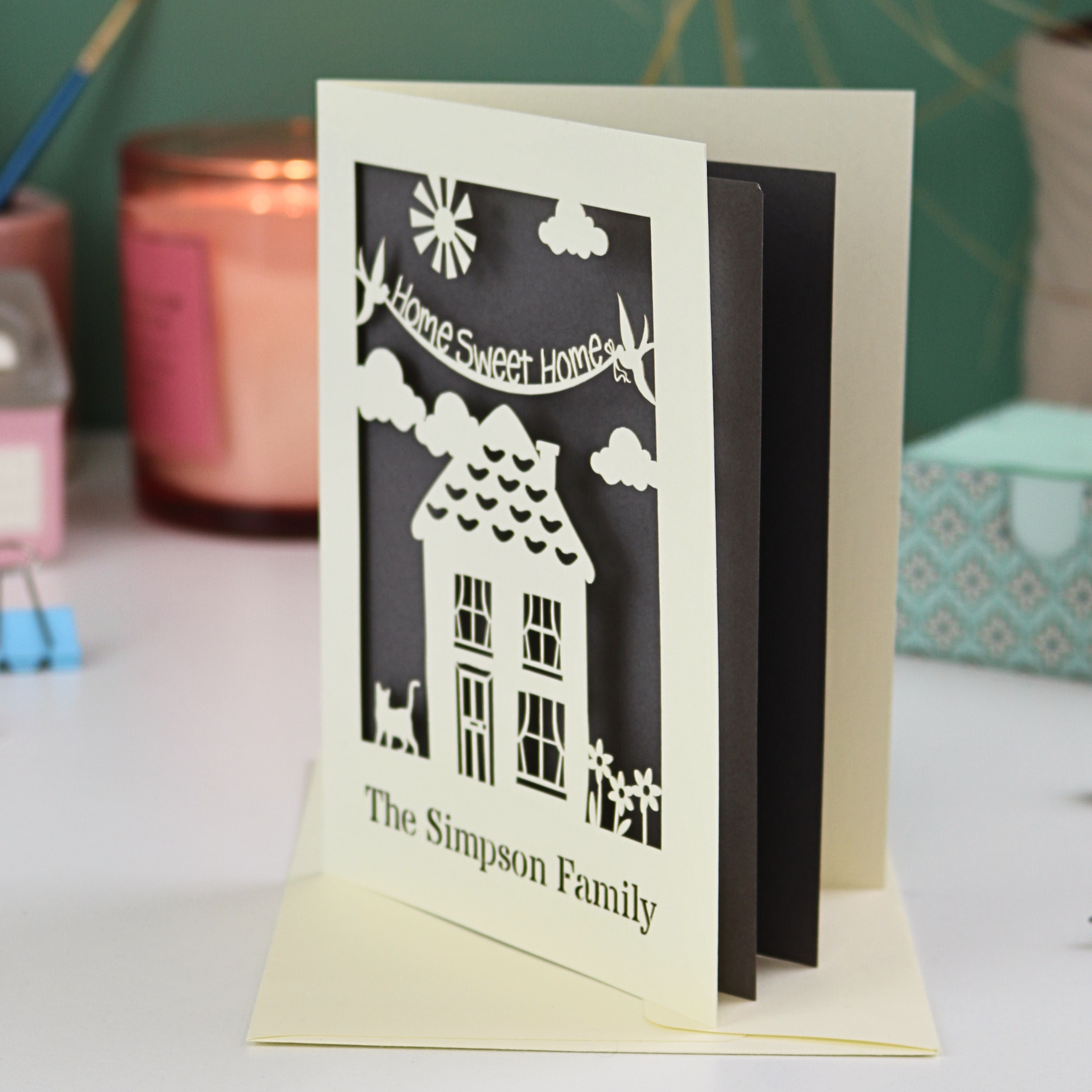 A laser cut new home card with cut out house design and the words "home sweet home" and personalised with the name of the recipients underneath