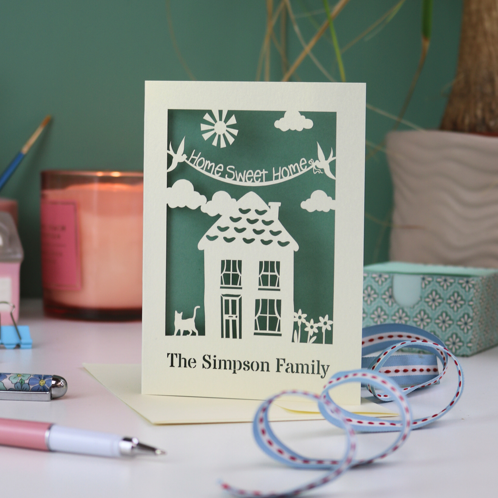 A laser cut new home card with cut out house design and the words "home sweet home" and personalised with the name of the recipients underneath