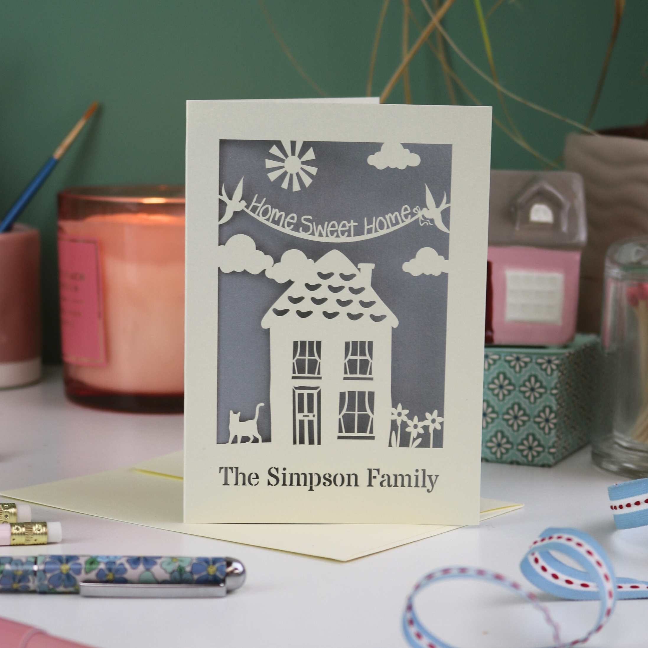 A laser cut new home card with cut out house design and the words "home sweet home" and personalised with the name of the recipients underneath