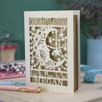 Personalised Congratulations Card with laser cut crescent moon design and text 'Congratulations, Over the moon for you Megan' on a wooden surface.