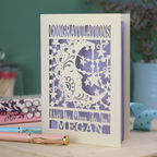 Personalised Congratulations Card with laser cut crescent moon design and text 'Congratulations, Over the moon for you Megan' on a wooden surface.