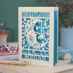 Personalised Congratulations Card with laser cut crescent moon design and text 'Congratulations, Over the moon for you Megan' on a wooden surface.