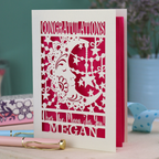Personalised Congratulations Card with laser cut crescent moon design and text 'Congratulations, Over the moon for you Megan' on a wooden surface.