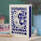 Personalised Congratulations Card with laser cut crescent moon design and text 'Congratulations, Over the moon for you Megan' on a wooden surface.