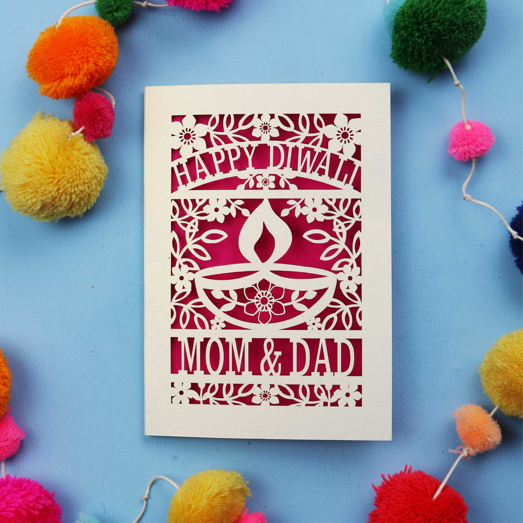 Decorative Diwali card with 'Happy Diwali' and 'Mom & Dad' text on a blue background with colourful pom-poms.