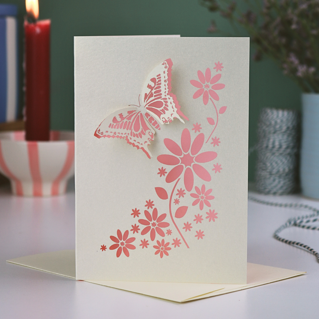 Card with butterfly and floral design on a table with candles and plants in the background