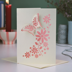 Card with butterfly and floral design on a table with candles and plants in the background