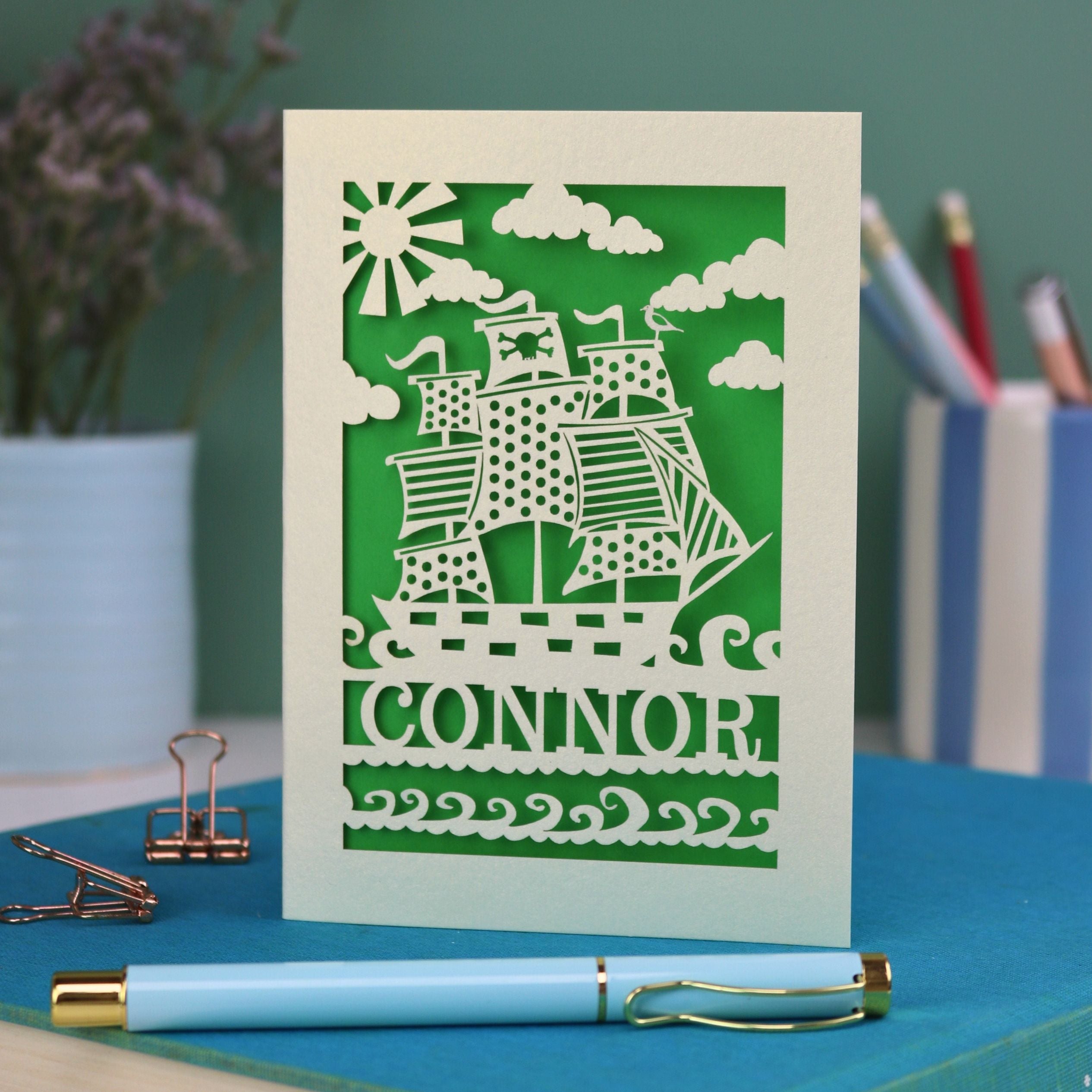 A personalised laser cut boys' birthday card with cut out pirate ship illustration and the name Alfie 