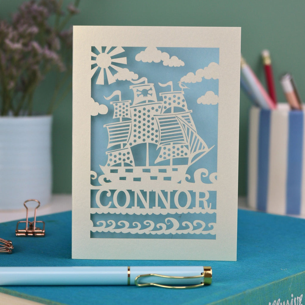 A personalised laser cut kids birthday card with cut out pirate ship illustration and the name Alfie 