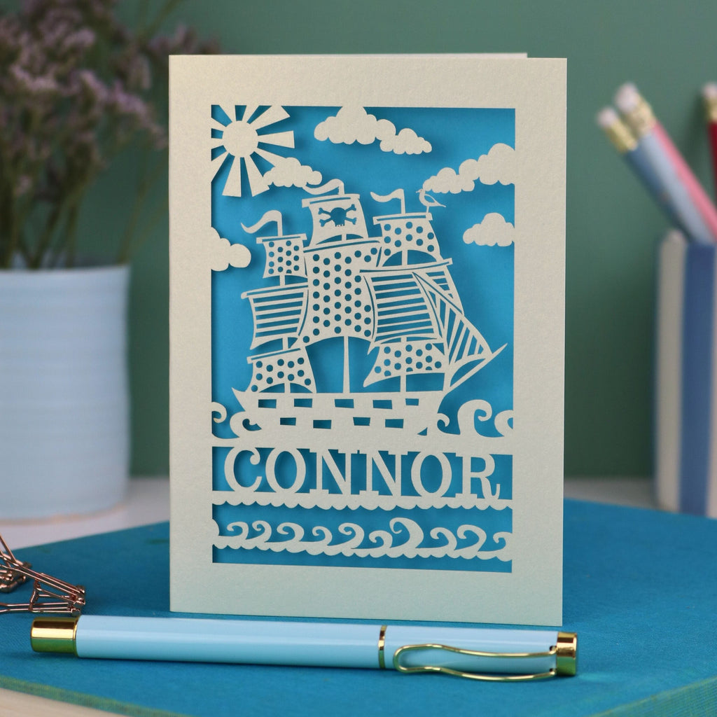 A personalised laser cut birthday card with cut out pirate ship illustration and the name Alfie 