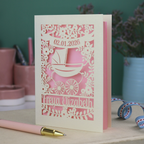 A personalised new baby card with laser cut floral vintage pram design. The baby's date of birth is cut out in stencil lettering in a banner, and the baby's name is at the bottom of the card.