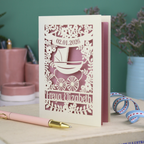 A personalised new baby card with laser cut floral vintage pram design. The baby's date of birth is cut out in stencil lettering in a banner, and the baby's name is at the bottom of the card.