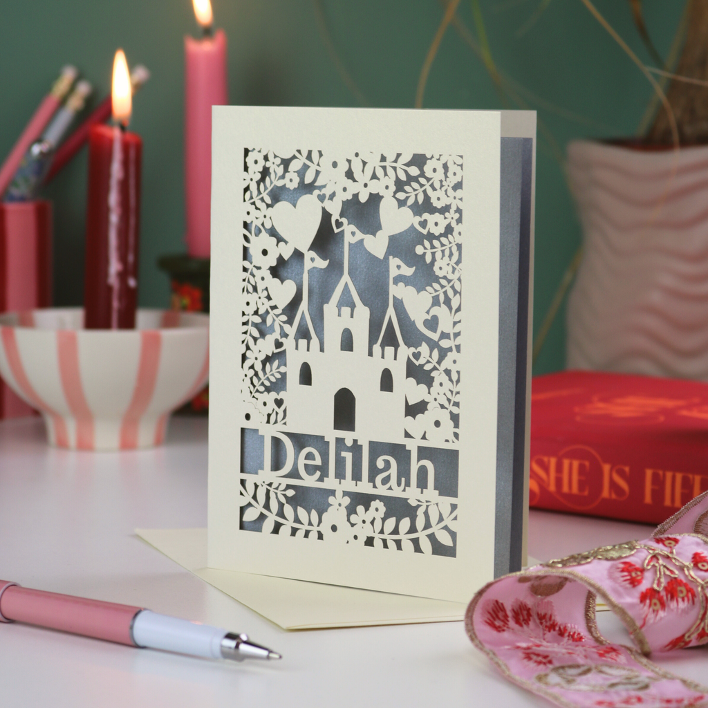 Decorative girl's birthday card with laser-cut design on a table with candles and stationery.