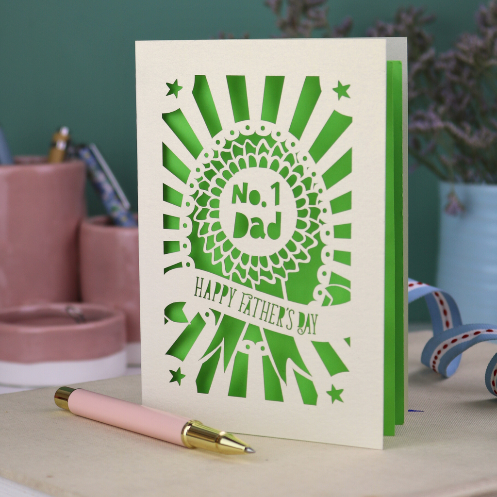 A laser cut cream Father's Day card with cut out rosette design and "No. 1 Dad" in the centre, and a banner with "Happy Father's Day" underneath. 