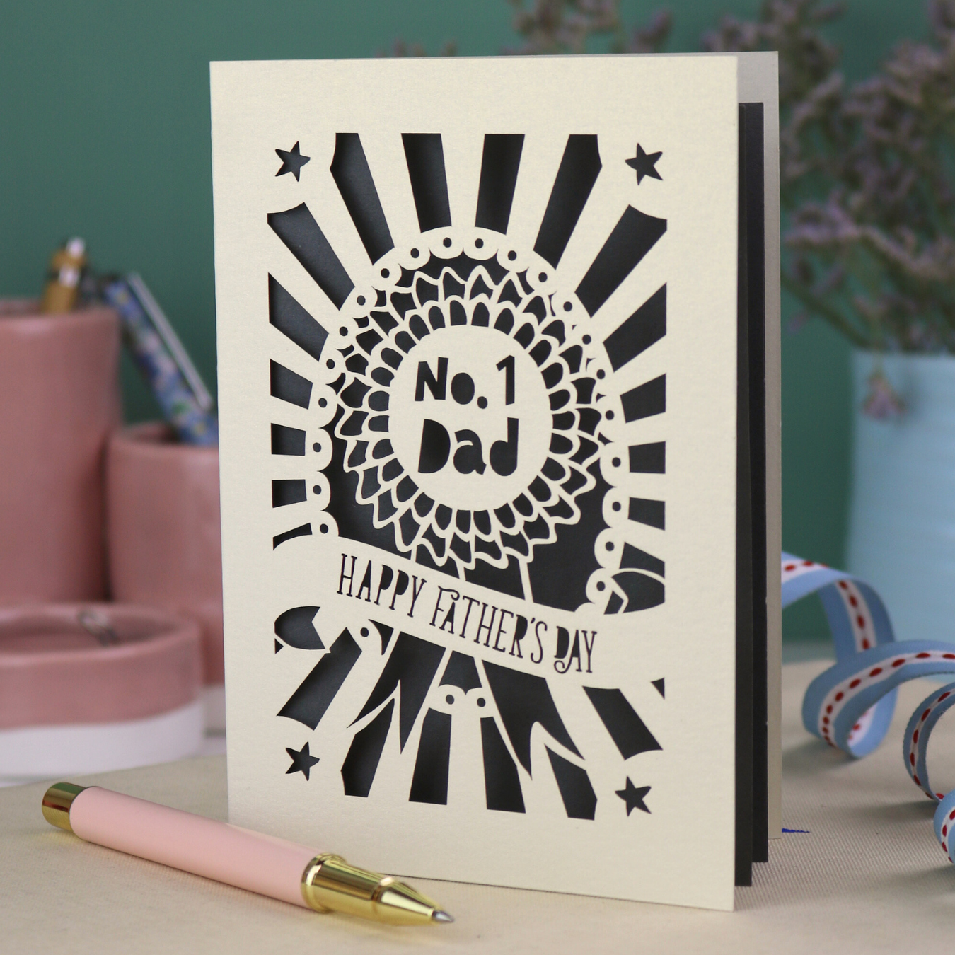 A laser cut cream Father's Day card with cut out rosette design and "No. 1 Dad" in the centre, and a banner with "Happy Father's Day" underneath. 