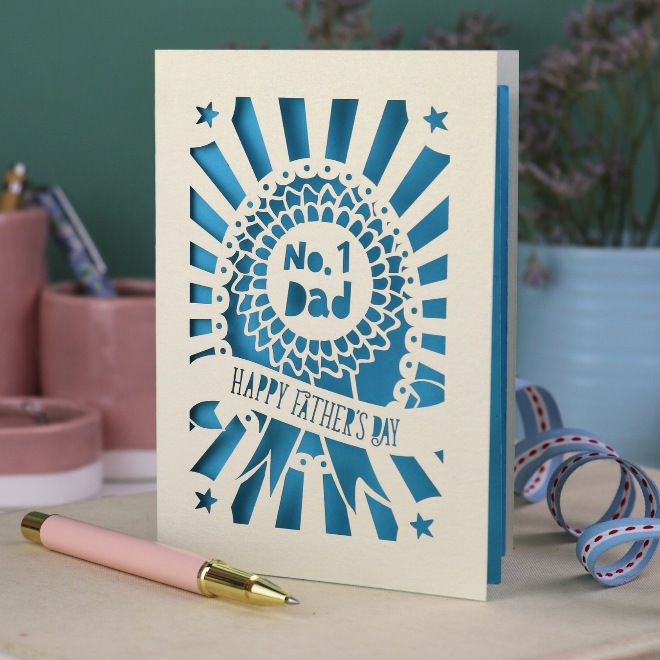 A laser cut cream Father's Day card with cut out rosette design and "No. 1 Dad" in the centre, and a banner with "Happy Father's Day" underneath. 