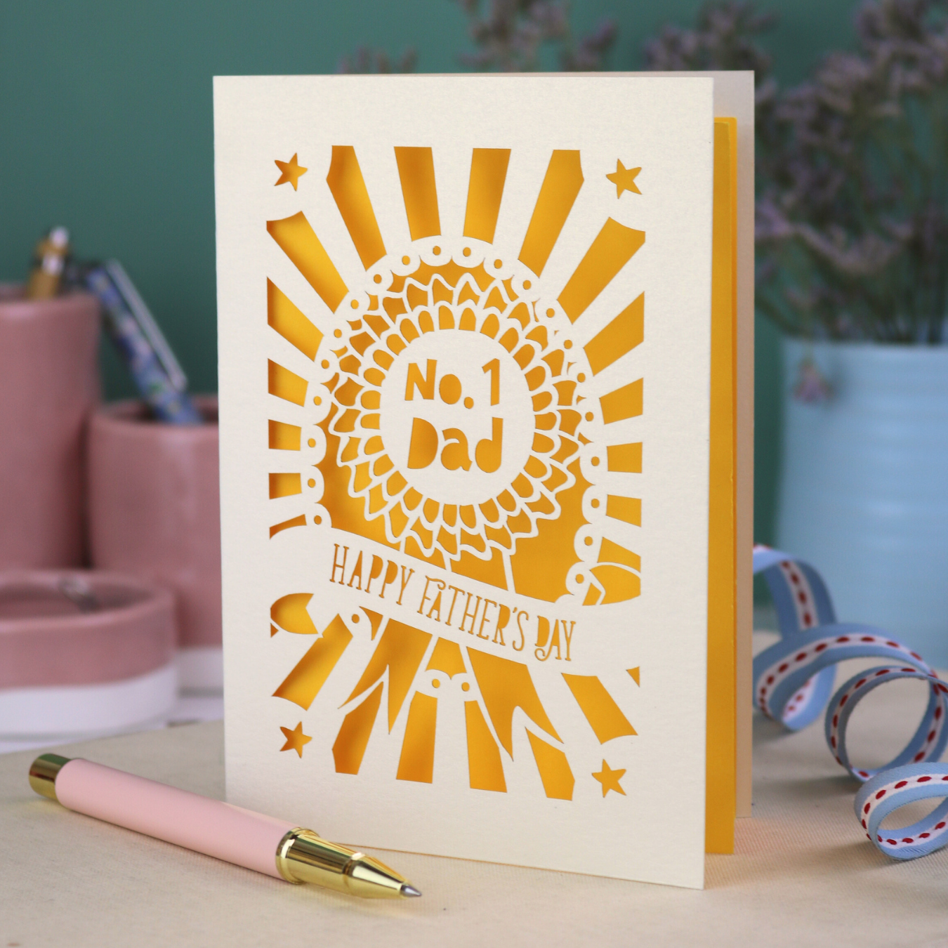 A laser cut cream Father's Day card with cut out rosette design and "No. 1 Dad" in the centre, and a banner with "Happy Father's Day" underneath. 