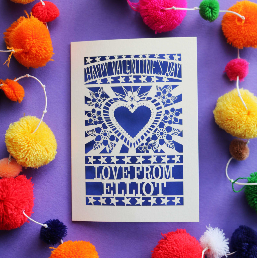 A personalised cut out Valentines card that has a heart and flowers cut out and text that says "Happy Valentine's Day, love from" and a name